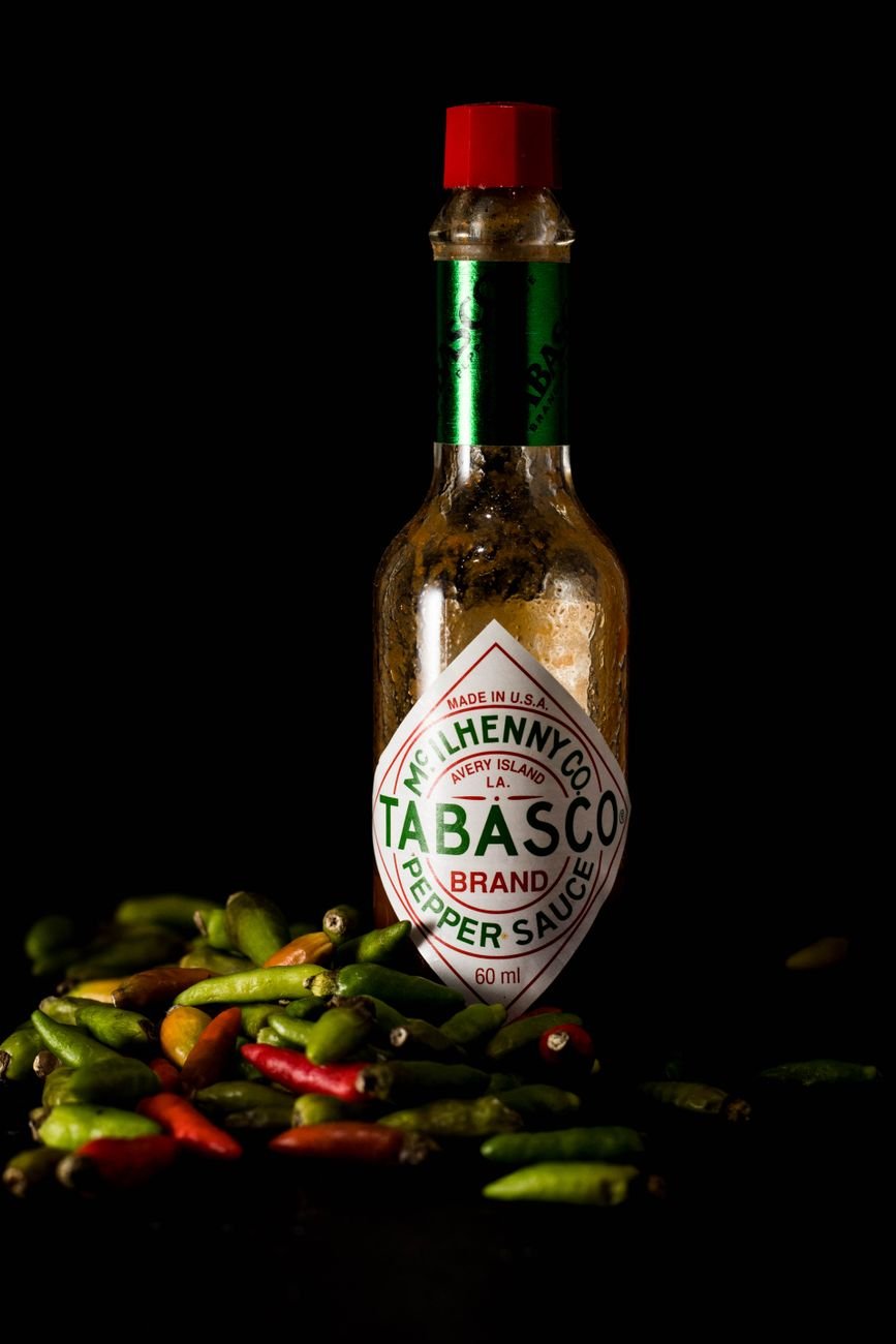 Close-up of a craft hot sauce bottle surrounded by fresh chilies on a black background